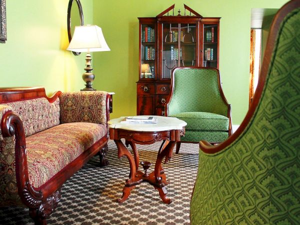 A vintage-style living room with ornate furniture, including a sofa, armchairs, a wooden cabinet, and a small table with a lamp.