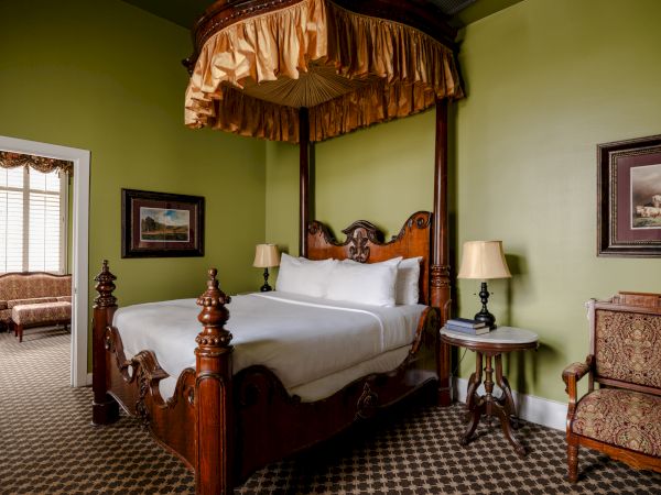 A luxurious vintage bedroom with a four-poster bed, green walls, ornate wood furniture, and classic lamps.