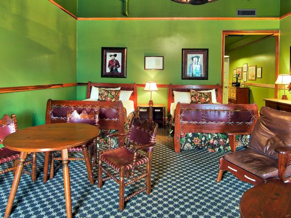 A green-walled room features wooden furniture, including tables, chairs, and beds, with patterned upholstery and framed art on the walls.