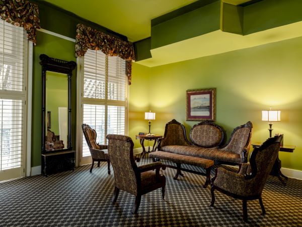 A vintage-style living room with green walls, wicker furniture, a matching coffee table, and warm lighting in a cozy seating arrangement.