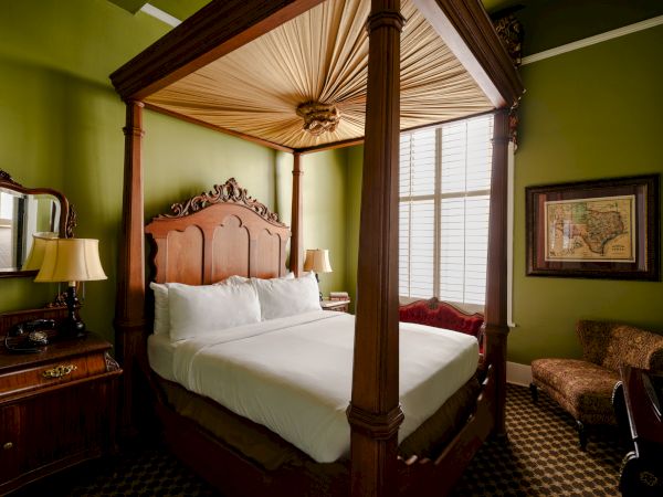 Luxurious four-poster bed with carved headboard in a green-walled hotel room, ornate lamps, and classic furnishings.