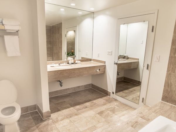 A modern bathroom features a toilet, sink with a large mirror, shelving with towels, and beige tiles throughout the room for a sleek look.