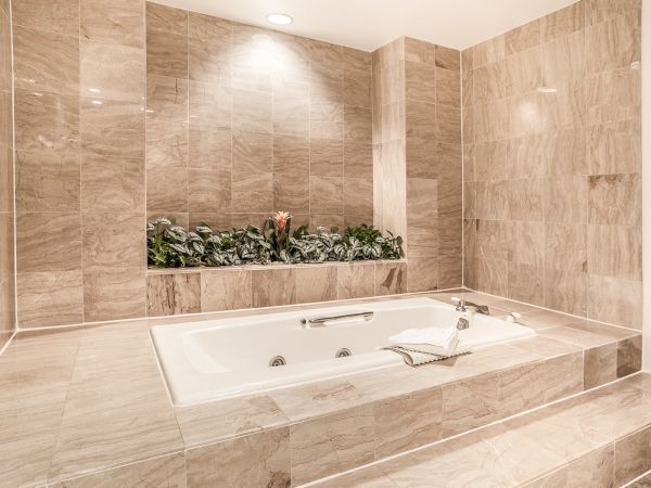 A luxurious bathroom with marble tiles features a sunken jacuzzi tub, greenery, and soft lighting for a relaxing atmosphere.