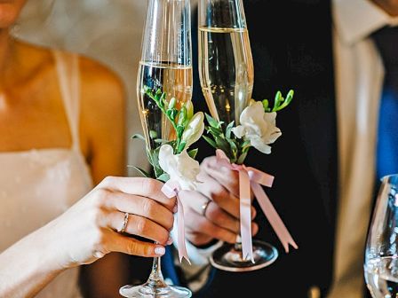 A couple toasting with champagne flutes, wedding vibe, flowers, and elegant attire.