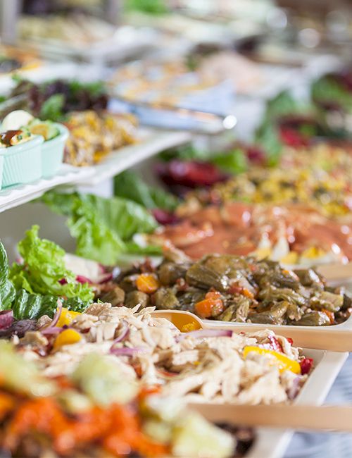 A line of colorful buffet dishes on a long table, with assorted salads, toppings, and hot dishes served in trays and wooden spoons.