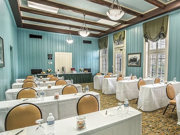 A bright, vintage-style conference room with turquoise walls, wooden beams, round and long tables set with white linens, chairs, and water bottles, ready for a meeting.