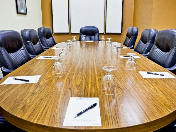A long oval wooden conference table in a boardroom, set with notebooks, pens, glasses, and chairs around it, ready for a meeting.