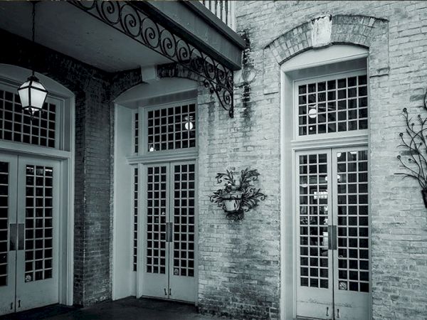 An old brick building with arched windows and French doors, a lantern, and decorative wrought-iron fixtures along the entryway.