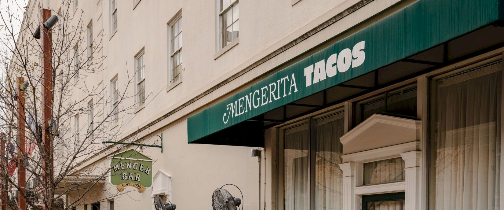 A cozy outdoor cafe with colorful metal chairs along a sidewalk, under a green awning that reads 'ARICERITA TACOS' in a city setting.