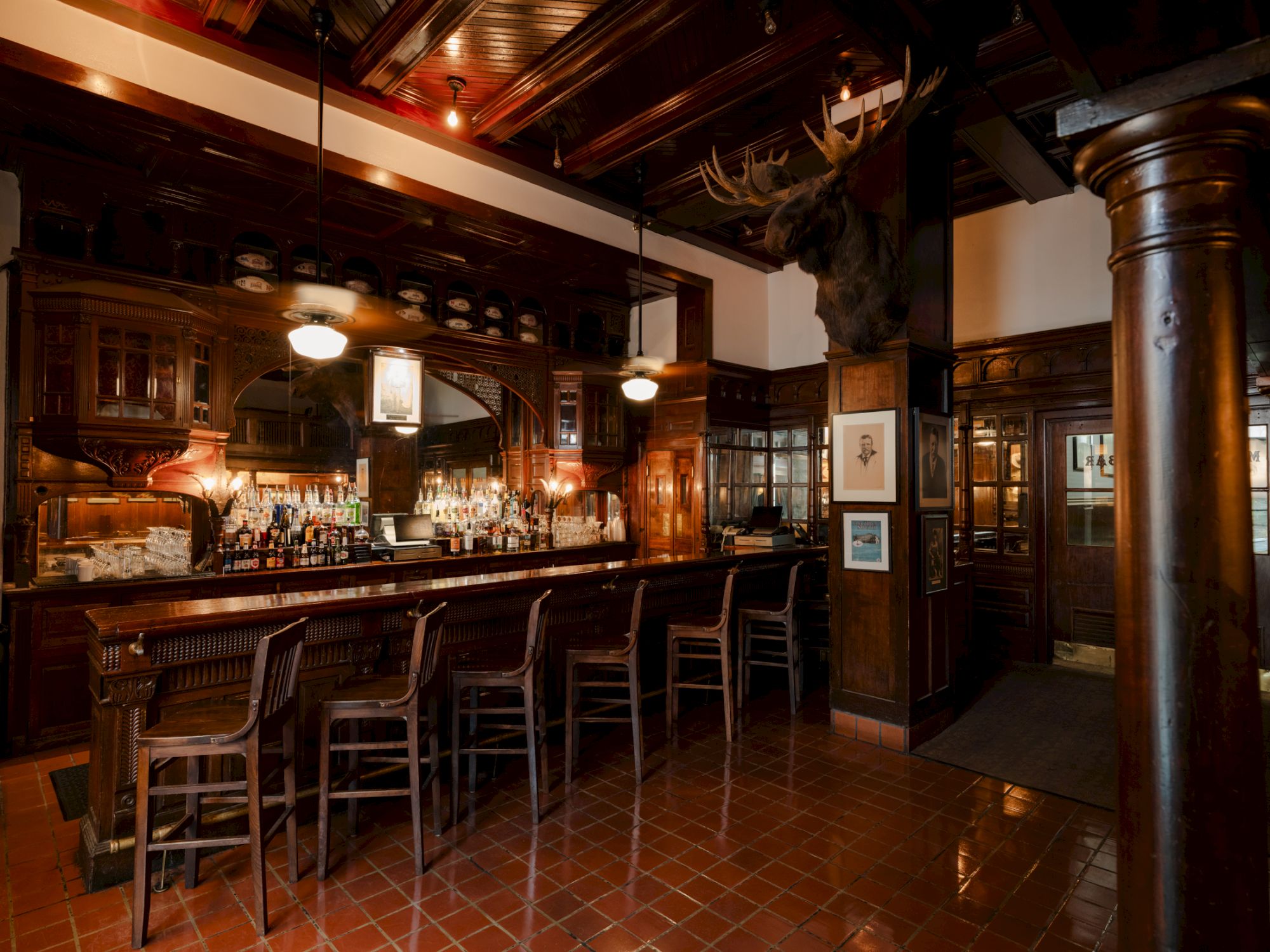 A cozy, dimly lit bar with wooden stools, a polished counter, warm lighting, and dark wood paneling creating a classic pub atmosphere.