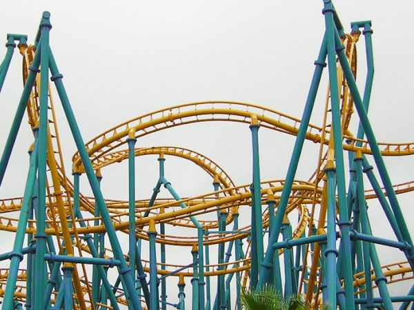 A tangled rollercoaster with blue supports and yellow tracks twisting above, chaotic loops and sharp turns in an amusement park.