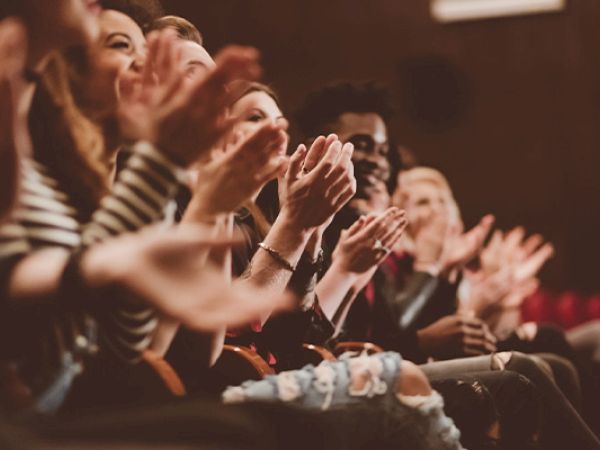 A row of people in an audience clapping and cheering, hands raised and smiling, enjoying a live performance or event.