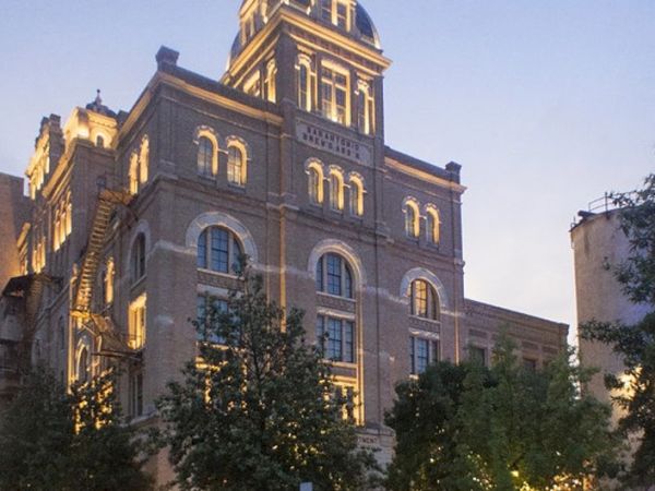 A large historic brick building with arched windows, ornate detailing, and a tower-like top, framed by trees at dusk. End.