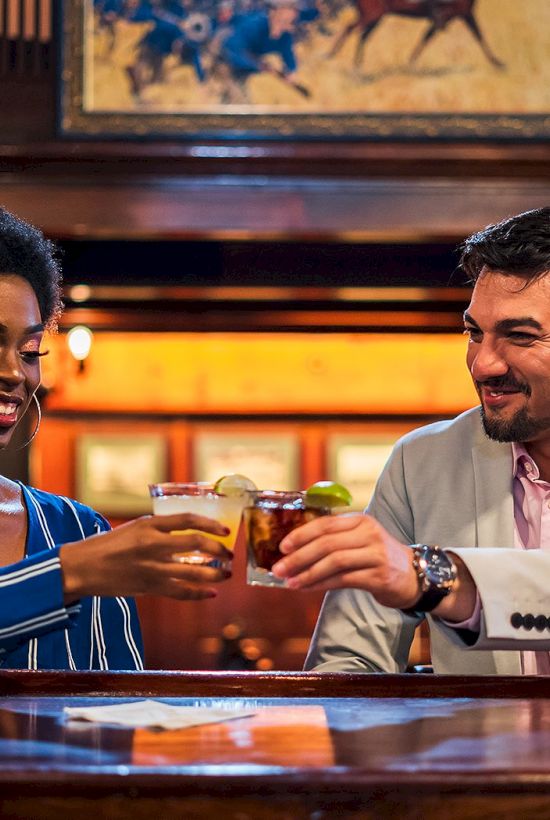 Two people in a bar smile and clink glasses, toasting together over drinks.