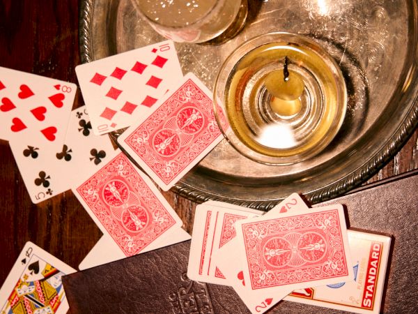 A poker spread with playing cards around a tray of drinks and a lit candle on a wooden table.
