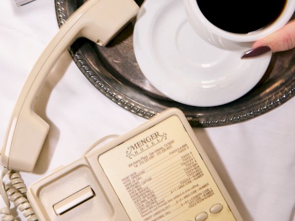 A hand-holding cup of coffee sits on a table beside a hotel phone and an open brochure of a lavish interior.