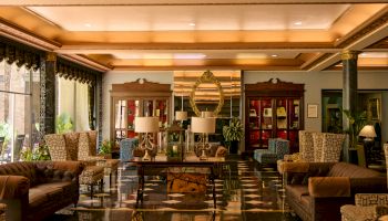 An elegant hotel lobby with plush sofas, lamps, ornate mirror, marble floor, and tall gold columns.