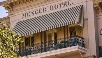 The Menger Hotel building facade with a striped awning and balconies in front.