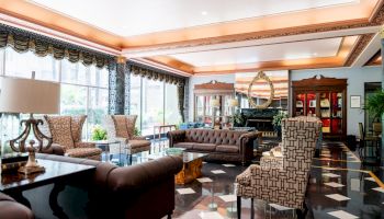 Luxurious hotel lobby with marble floors, tufted sofas, patterned chairs, large windows, warm lighting, and elegant decor. Great waiting area.