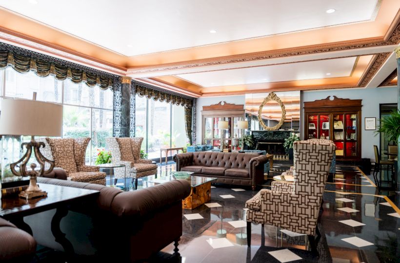 Luxurious hotel lobby with marble floors, tufted sofas, patterned chairs, large windows, warm lighting, and elegant decor. Great waiting area.