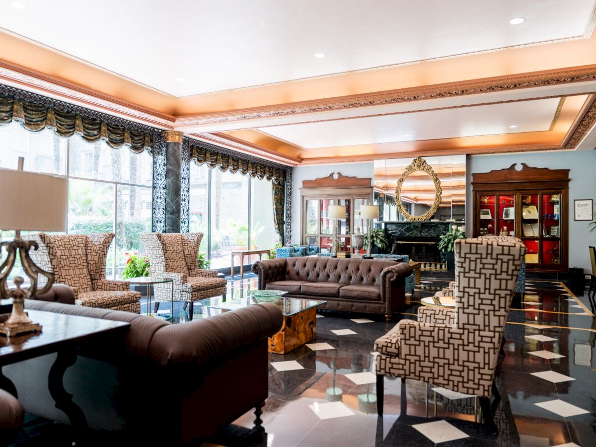 A luxurious hotel lobby with plush seating, marble floors, and elegant decor; bright natural light via windows, stylish lamps, and artful accents.
