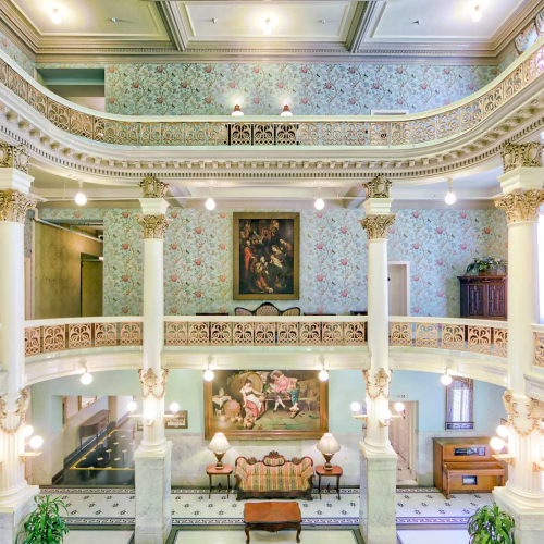 A grand, ornate European-style living room with marble floors, gilded moldings, a central fireplace, and elegant chandeliers.