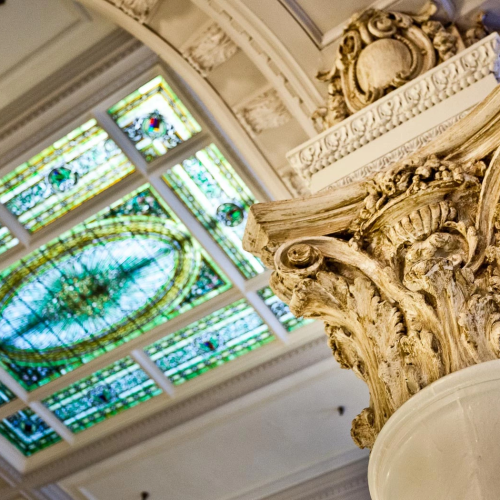 A grand, ornate ceiling with gold accents and a colorful central mural, supported by arches and detailed architectural carvings.