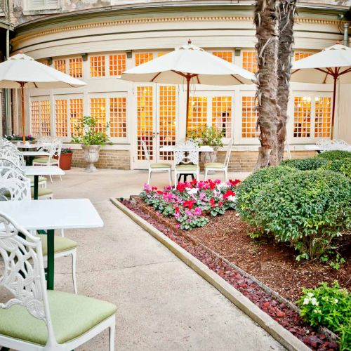 A cozy outdoor caf&eacute; scene with chalkboard menus, string lights, potted plants, and white patio furniture under a warm, inviting awning.