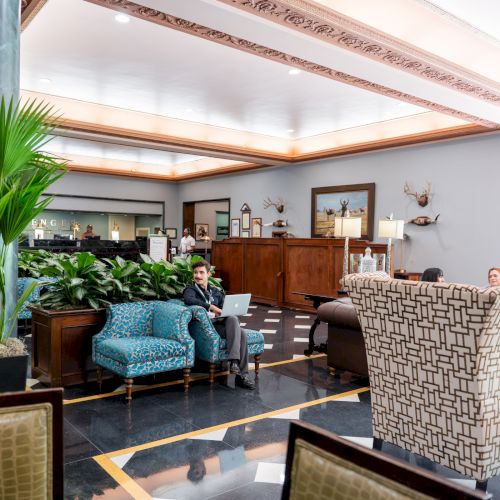 A bright, cozy living room with a teal sofa, plants, wooden coffee table, and warm sunlight streaming through large windows.