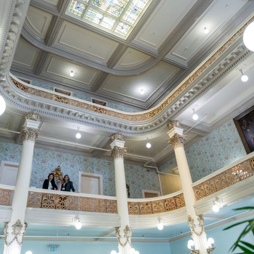 A grand, ornate ceiling with gilded moldings, chandeliers, and a bright skylight, suggesting a luxurious historic interior.
