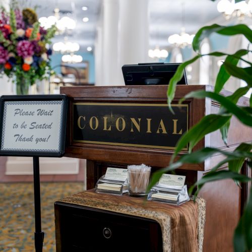 A small handmade sign reading &ldquo;OPEN&rdquo; sits on a wooden crate with light flowers and greenery in the background, cozy outdoor display.