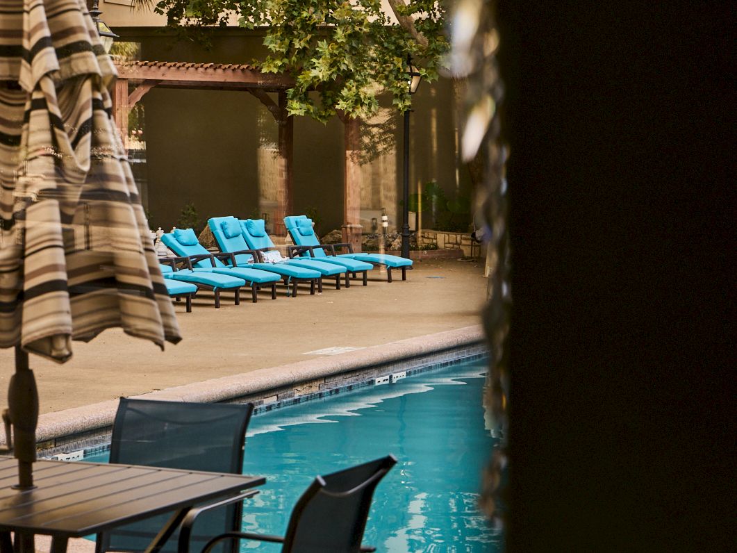 An outdoor pool courtyard with turquoise lounge chairs, framed by drapery and green vines in warm sunlight.