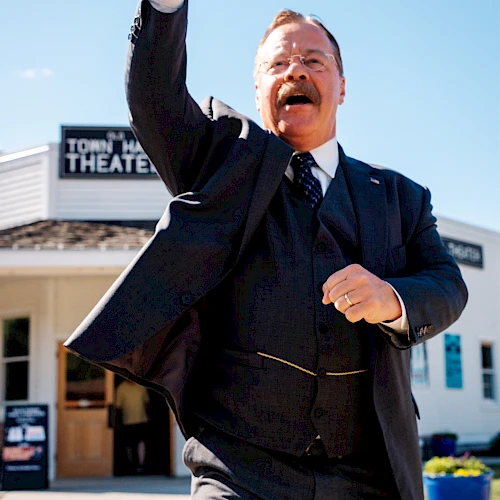 A man in a suit is cheering with a raised fist outside a theater, exuding triumph and celebration.