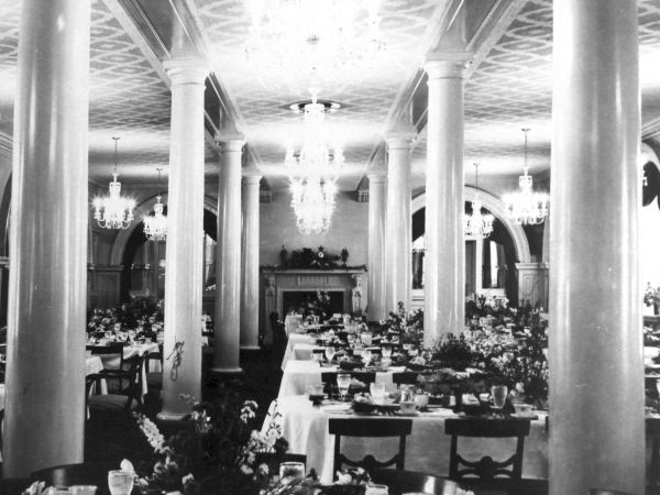 A grand, elegant dining hall with long tables set for a formal banquet, chandeliers, columns, and a classic, vintage vibe.