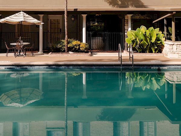 A peach-colored building with arched windows, green awnings, and a ground-floor cafe by a rectangular pool reflecting the facade.