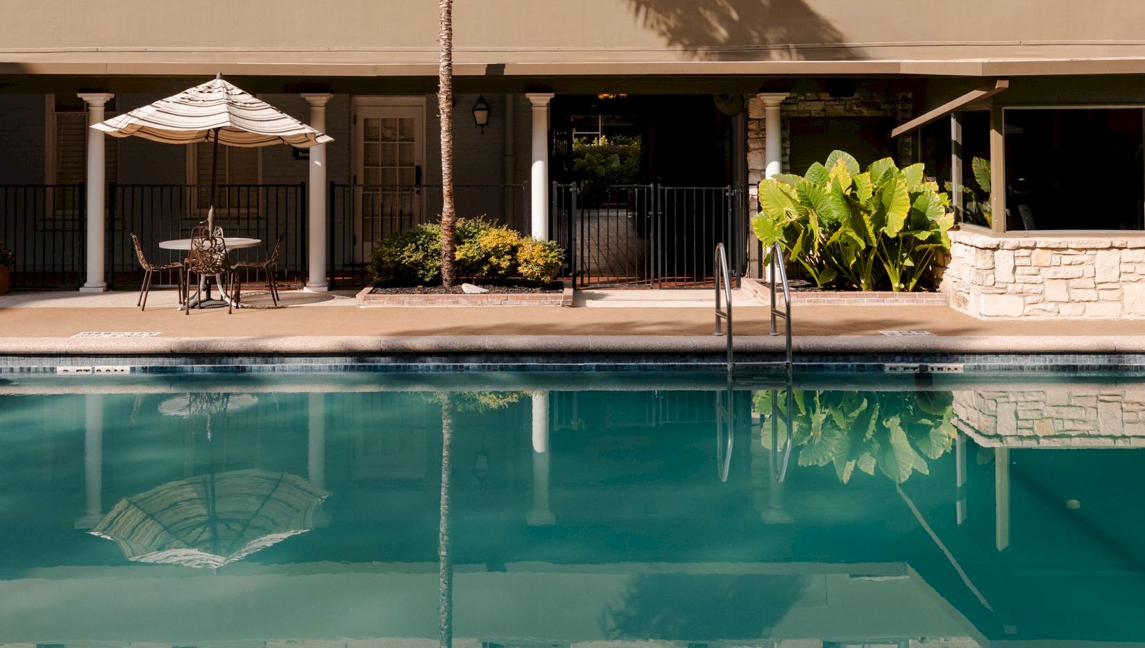 A stylish hotel facade with arched windows, balconies, and a ground-floor terrace; a calm outdoor pool reflects the building.