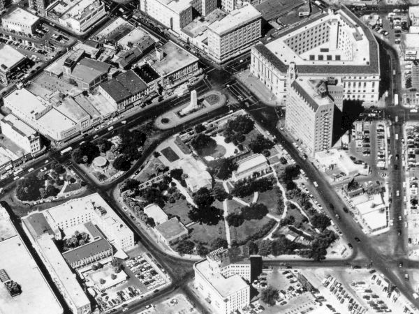 Aerial view of a city block with roads forming a circular park or plaza, surrounded by mid-rise buildings and dense urban layout.