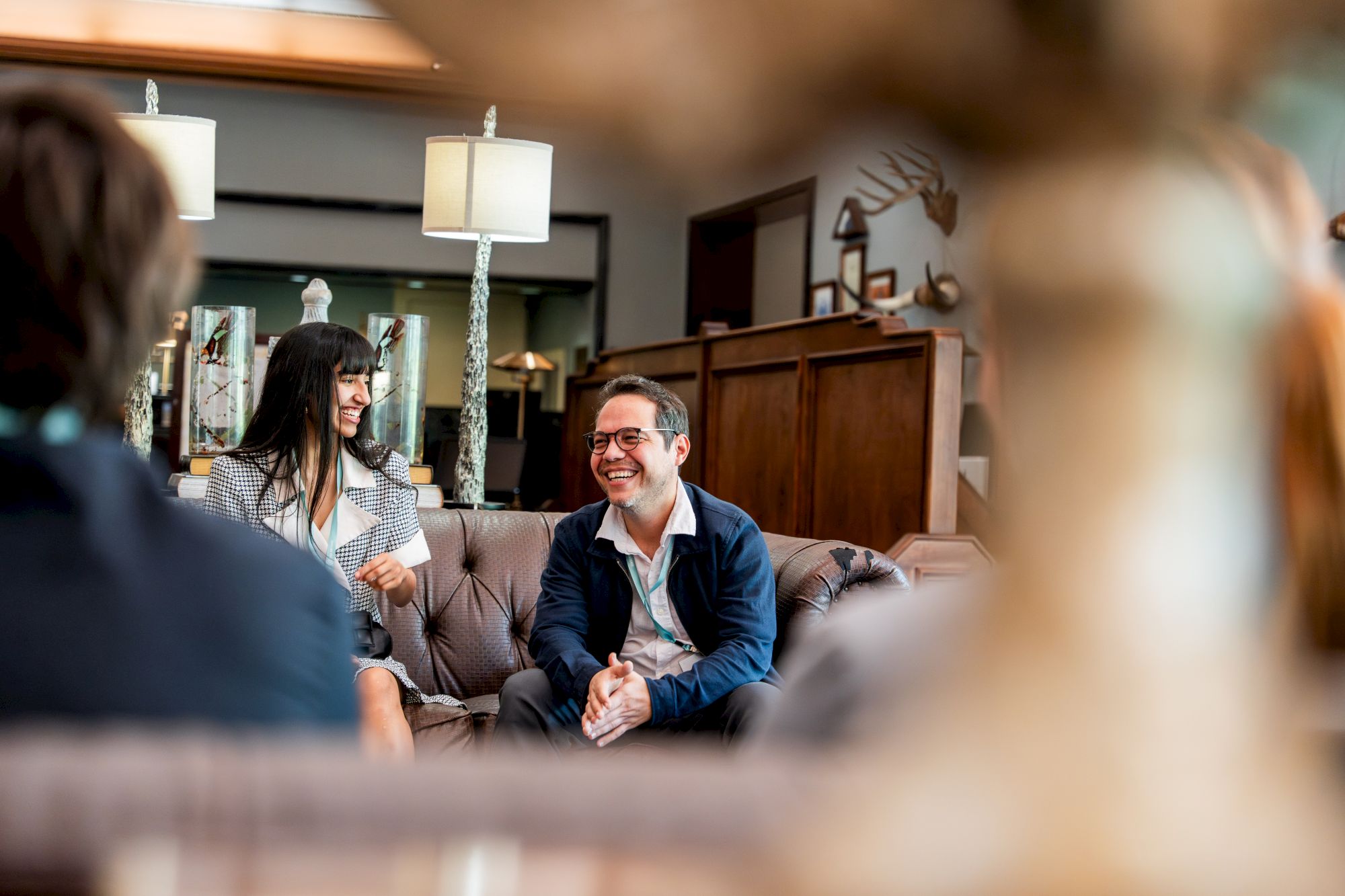 A group of friends chatting warmly in a cozy lounge, smiling and seated on a sofa with a modern, inviting interior.