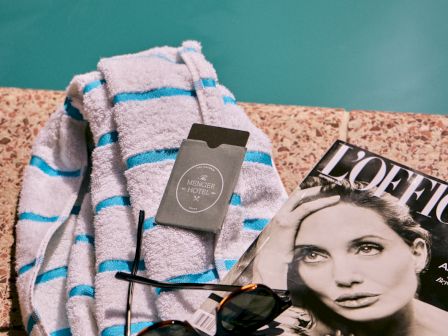 A folded blue-and-white striped robe with a black hotel card, sunglasses, and a fashion magazine on a teal background.