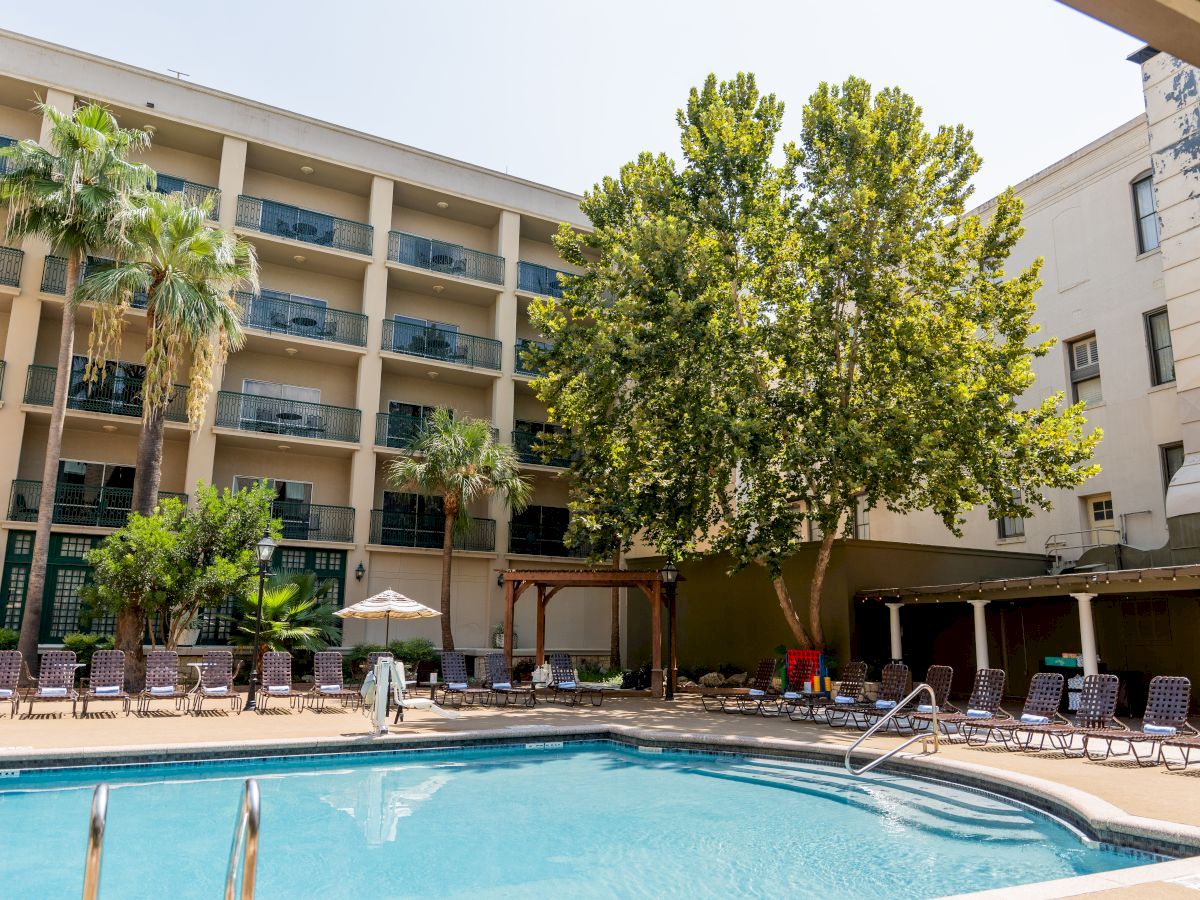 Outdoor hotel courtyard with a swimming pool, lounge chairs, and palm trees beside multi-story balconies.