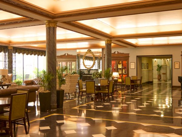 An elegant hotel lobby with marble flooring, tall columns, upholstered chairs, and a decorative mirror in warm lighting.