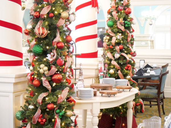 Indoor holiday buffet with decorated Christmas trees in red, green, and gold ornaments, lights, and bows.