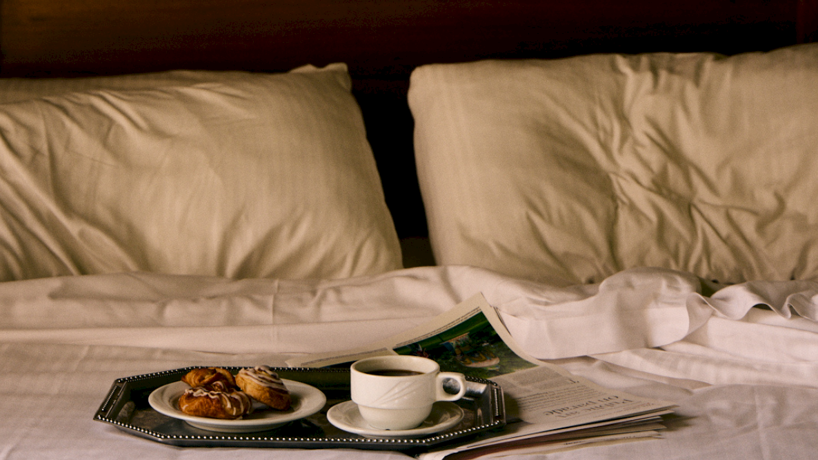 A made bed with pillows, a breakfast tray, a cup of coffee, and pastries spread out on top.
